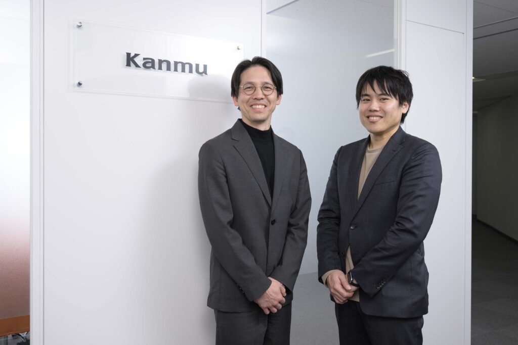 カンム様のロゴの前で立っているカット