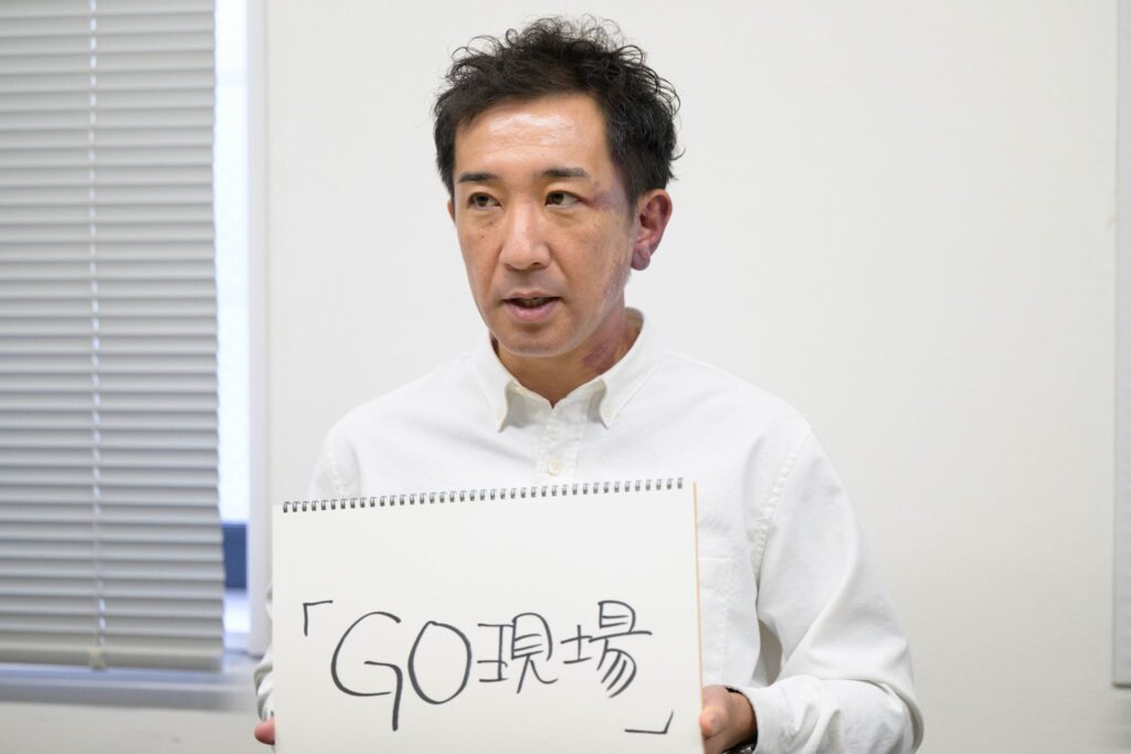 HQ稲垣さんが「GO現場」と書いたフリップを見せながら話をしているところ