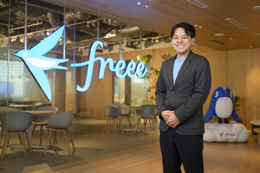 freeeのロゴの前に立つ正田さん