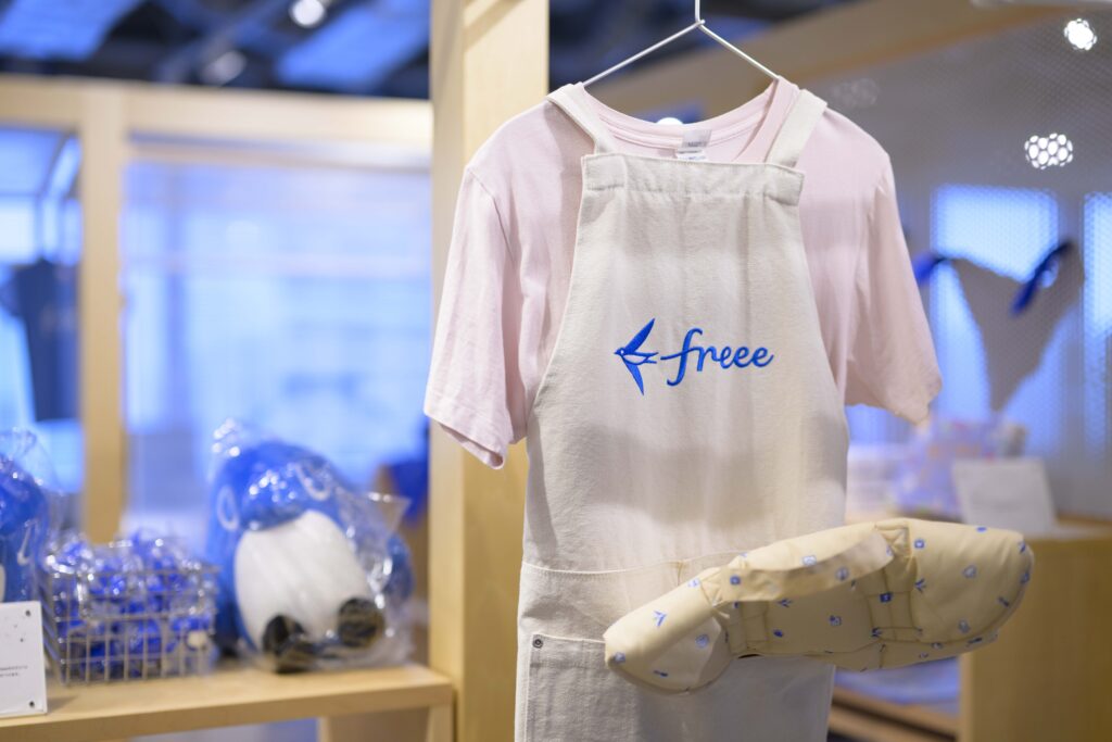 freeeのロゴ入りエプロンやグッズが並ぶオフィスの一角
