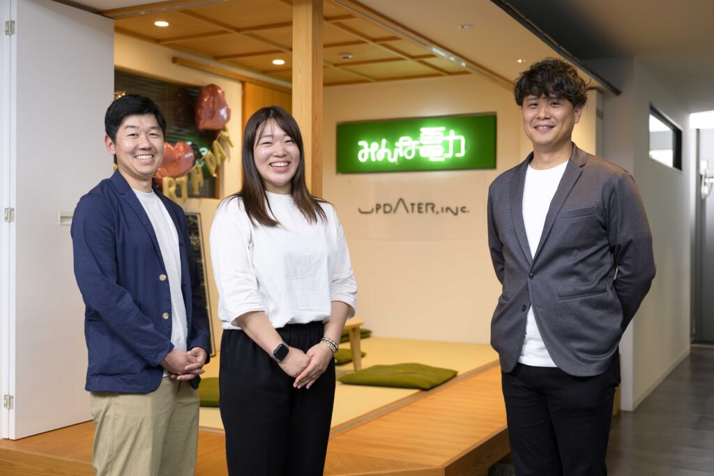 「みんな電力」のロゴサインを背に並ぶ坂本さん、松岡さん、遠藤さん